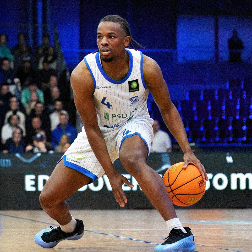 Un jugador de baloncesto dribla el balón en la cancha mientras lleva una camiseta a rayas con el número 4.